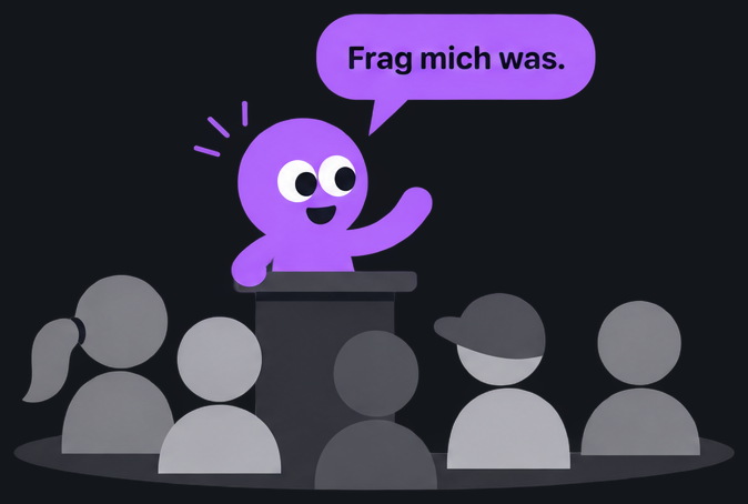 Qraki steht am Pult vor einer Klasse und sagt: Frag mich was.